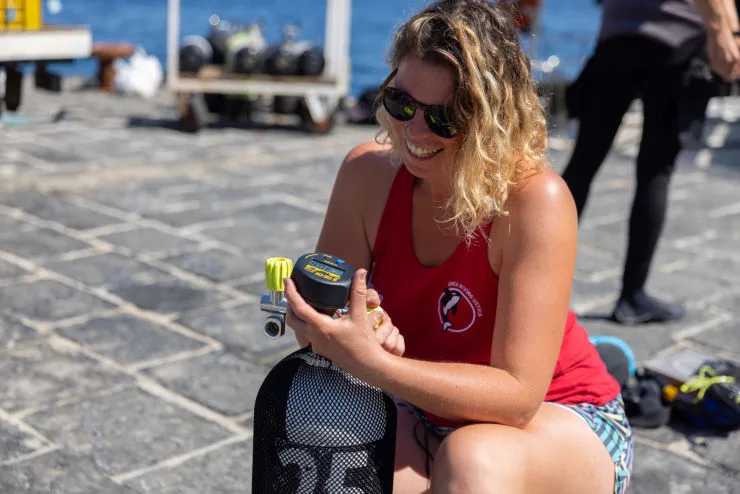 Plongeuse souriante vérifie un détendeur devant des bouteilles et un quai