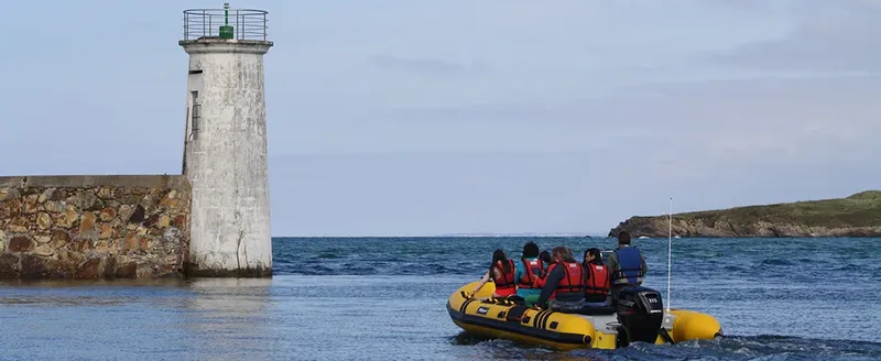 Un bateau pneumatique jaune avec des passagers navigue près d'un phare