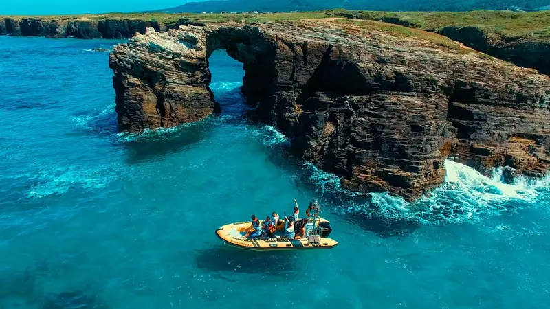 Un bateau semi-rigide avec des personnes navigue près de falaises rocheuses