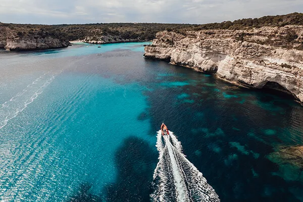Bateau rapide naviguant dans une crique turquoise entre falaises calcaires