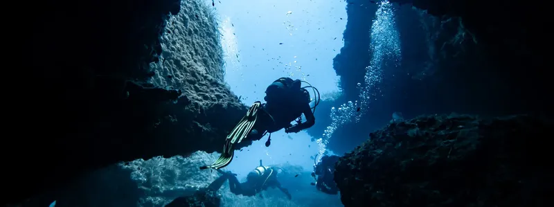 Deux plongeurs explorent une grotte sous-marine éclairée par le soleil