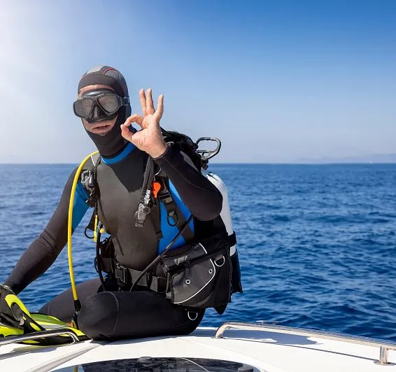 Plongeur en combinaison noire fait le signe OK sur un bateau