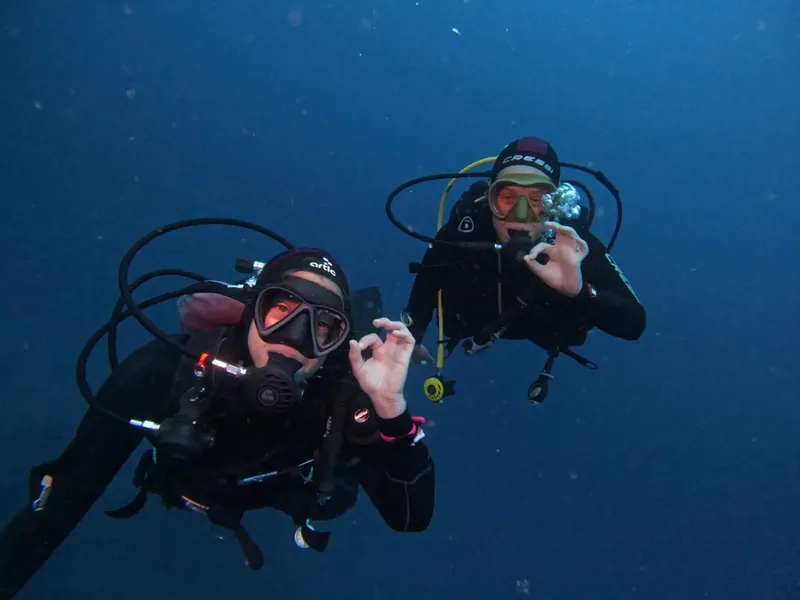Deux plongeurs souriants font un signe de la main sous l'eau