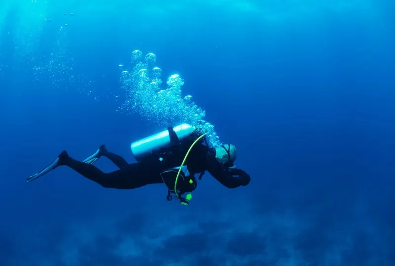 Plongeur en combinaison noire nageant dans une eau bleue claire