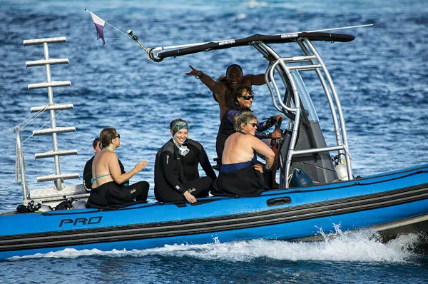 Groupe de plongeurs souriants à bord d'un bateau semi-rigide bleu