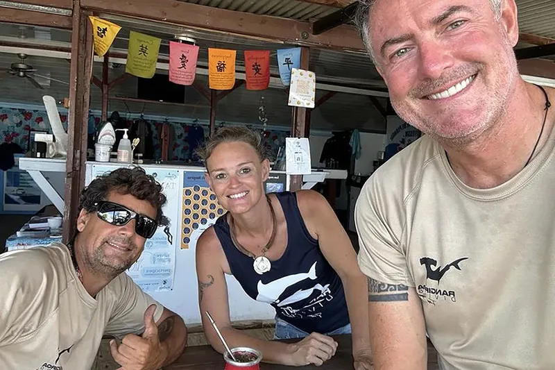 Trois personnes souriantes devant un comptoir avec du matériel de plongée