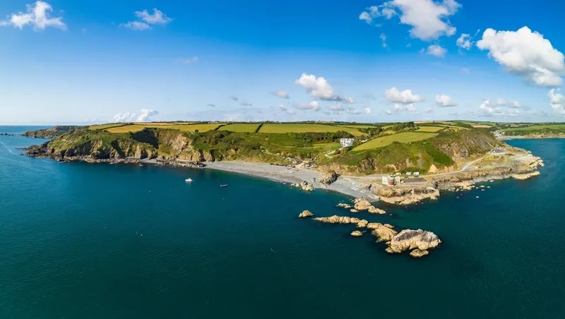 Côte rocheuse avec une plage, des champs verts et une mer bleue