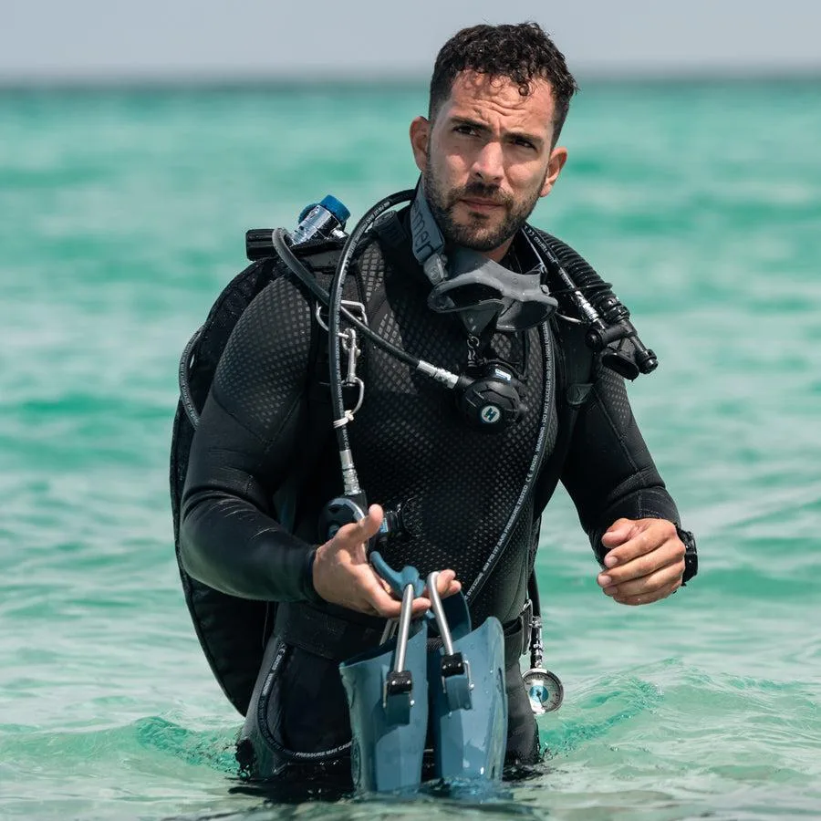 Plongeur en combinaison noire se prépare à entrer dans l'eau turquoise