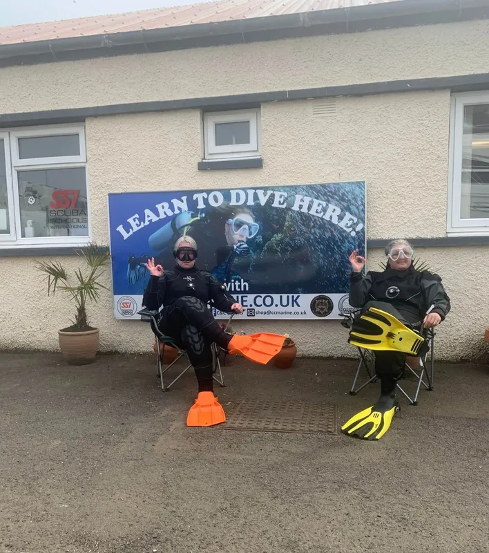 Deux plongeurs souriants en combinaison avec palmes devant un centre