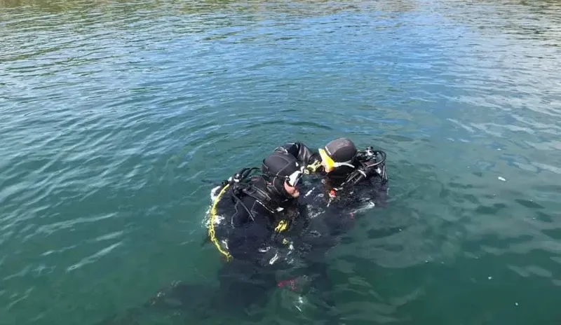 Deux plongeurs en combinaison s'entraident sous la surface de l'eau