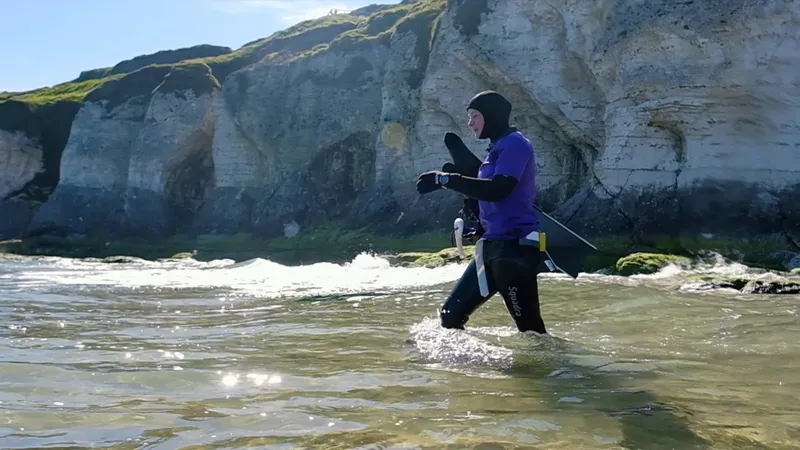 Plongeur en combinaison sort de l'eau sur une plage rocheuse