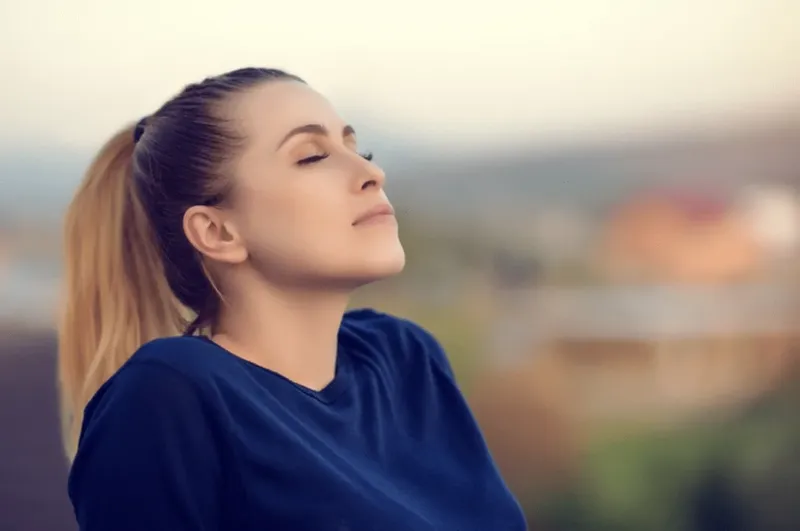 Jeune femme les yeux fermés, visage levé vers le ciel
