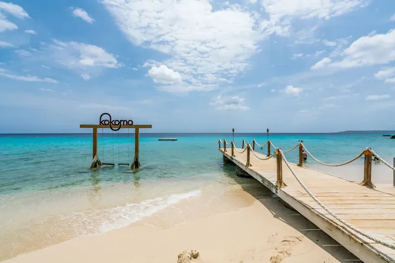 Plage de sable blanc, ponton en bois et structure avec le texte kokomo