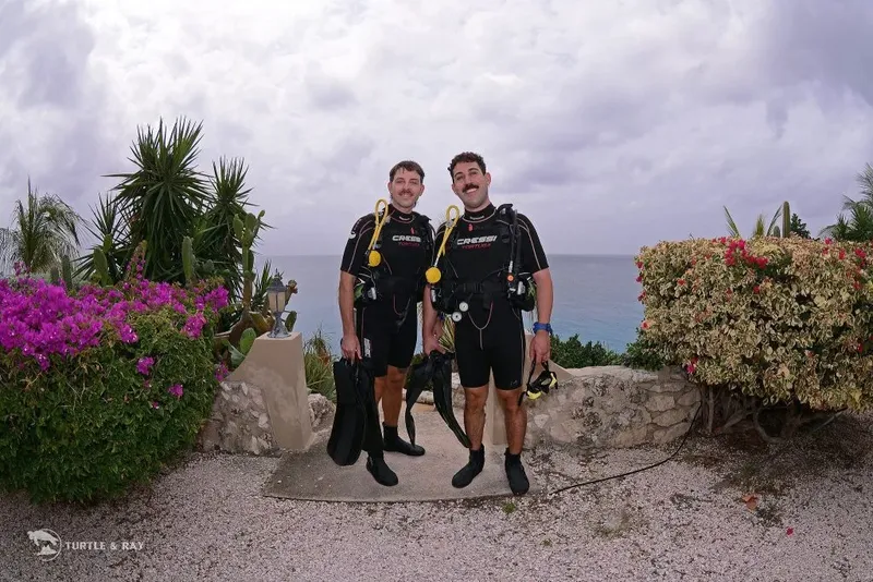 Deux plongeurs en combinaison, équipés, souriants devant la mer