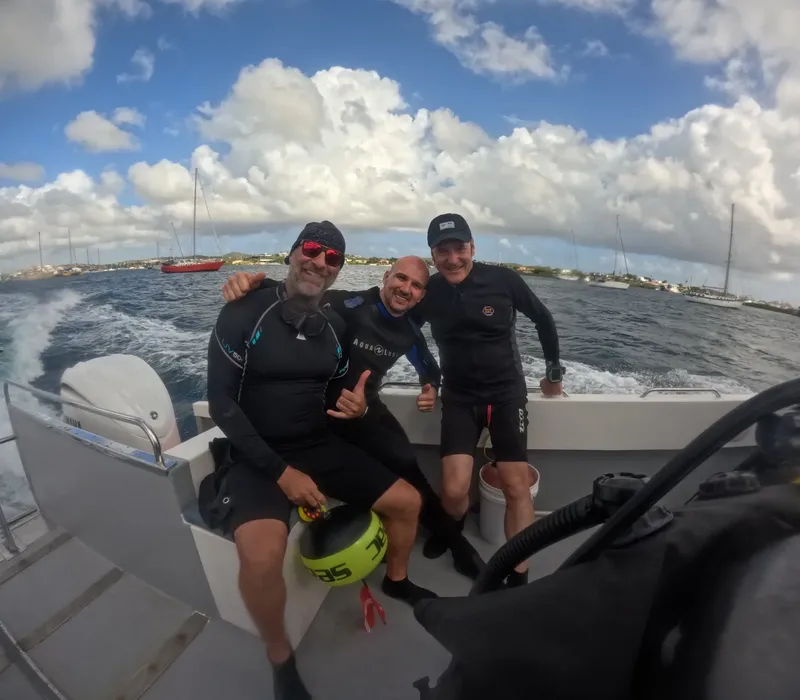 Trois plongeurs souriants sur un bateau en mer, ciel nuageux