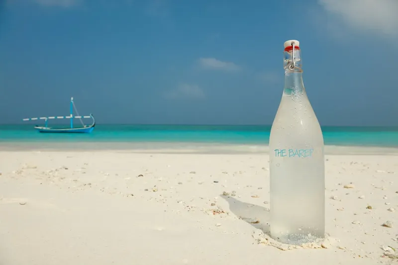 Bouteille en verre sur plage de sable blanc avec bateau au loin
