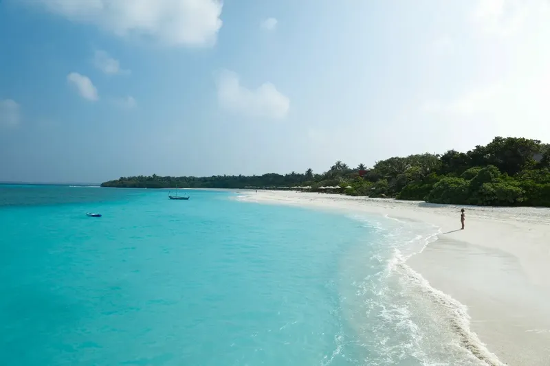 Plage de sable blanc, eau turquoise, personne se promène au bord de l'eau