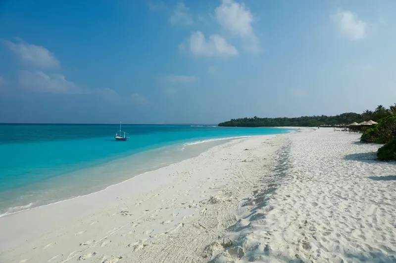 Plage de sable blanc, eau turquoise et bateau au large ciel bleu