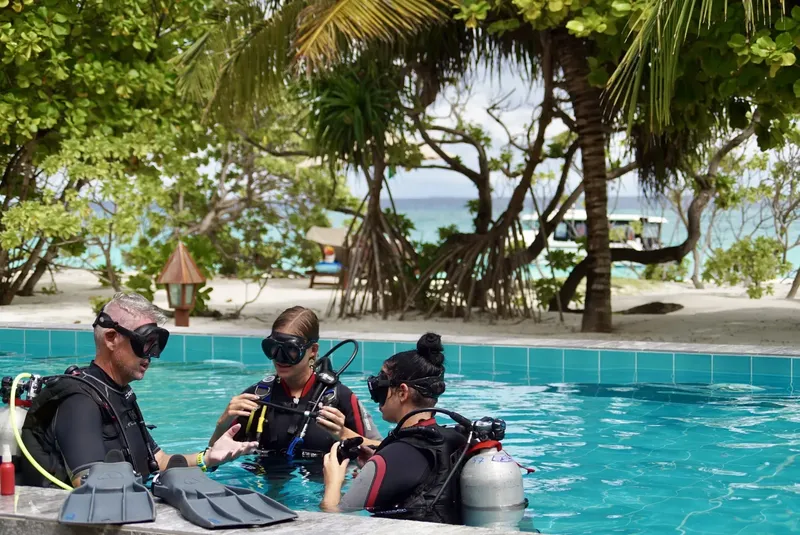 Trois plongeurs en formation dans une piscine, équipement complet visible