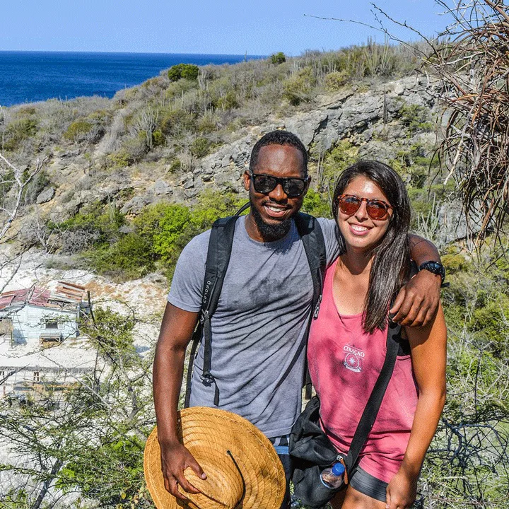 Couple souriant avec sacs à dos, paysage côtier en arrière-plan