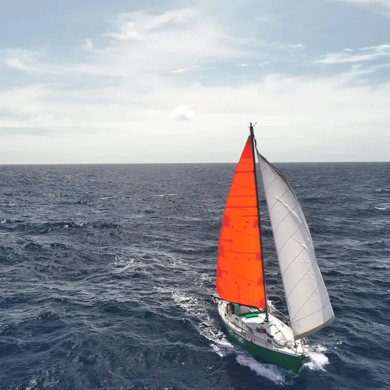 Voilier orange et blanc naviguant sur une mer agitée sous un ciel nuageux