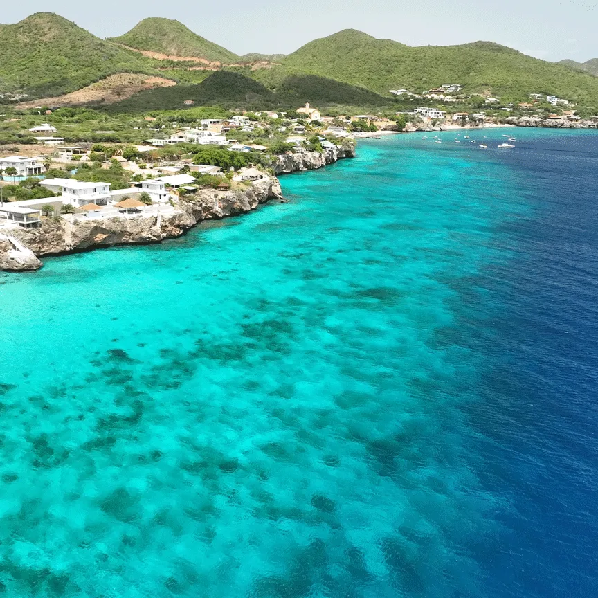 Côte rocheuse avec eau turquoise, bâtiments et collines verdoyantes