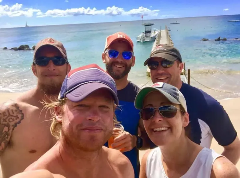 Groupe de personnes souriantes sur une plage avec un bateau au loin