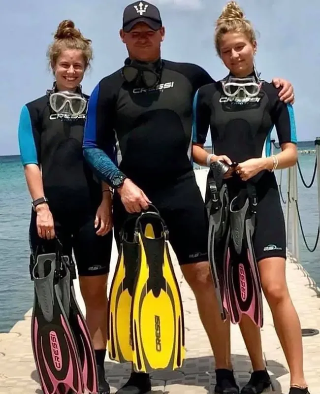 Trois plongeurs souriants en combinaison, palmes et masque sur un ponton