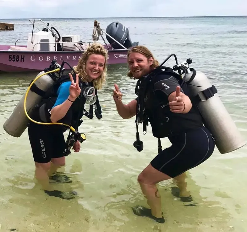 Deux plongeurs souriants avec leur équipement dans l'eau peu profonde