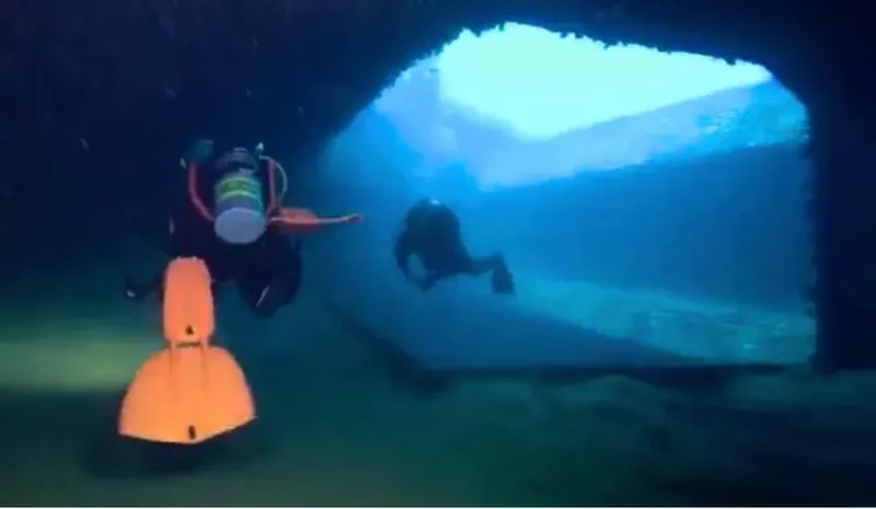 Deux plongeurs explorent une grotte sous-marine, lumière bleutée et visibilité