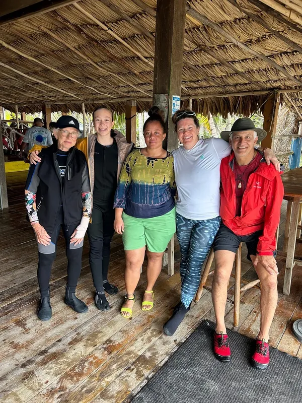 Groupe de cinq personnes souriantes posant devant une structure en bois