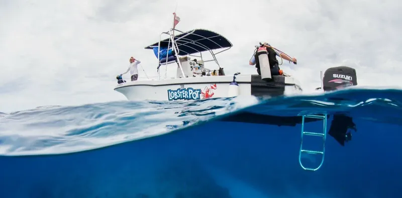 Bateau de plongée avec des plongeurs, vue mi-immergée, ciel nuageux