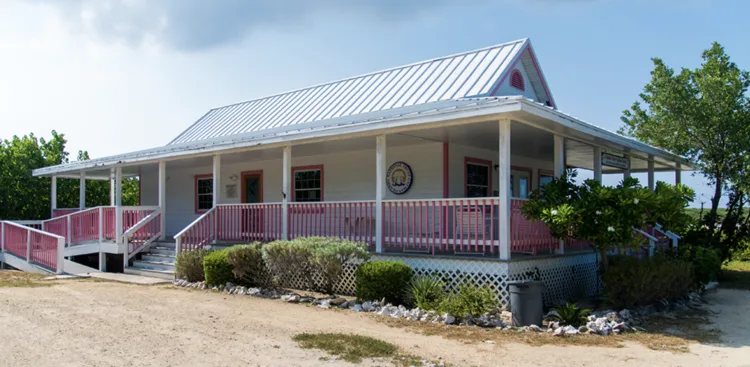 Bâtiment blanc avec véranda, végétation tropicale et ciel bleu clair