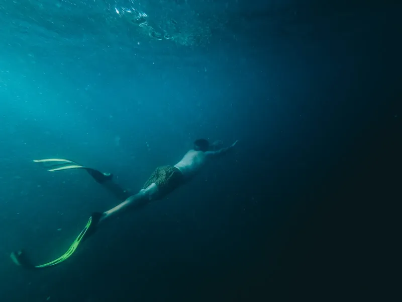 Un plongeur en apnée nage dans une eau bleu foncé et profonde