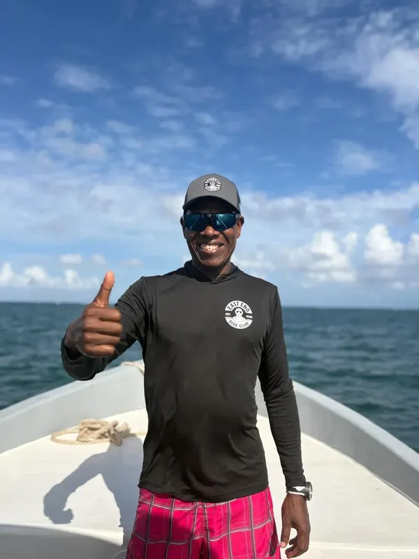 Homme souriant sur un bateau, pouce levé, ciel bleu en arrière-plan