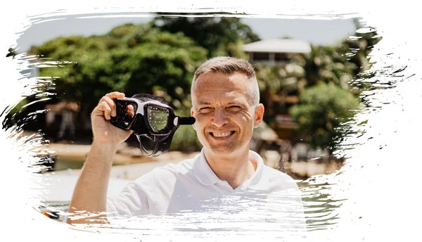 Homme souriant tenant un masque de plongée sur la plage