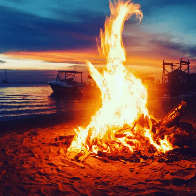 Feu de joie sur la plage avec bateaux et ciel coloré