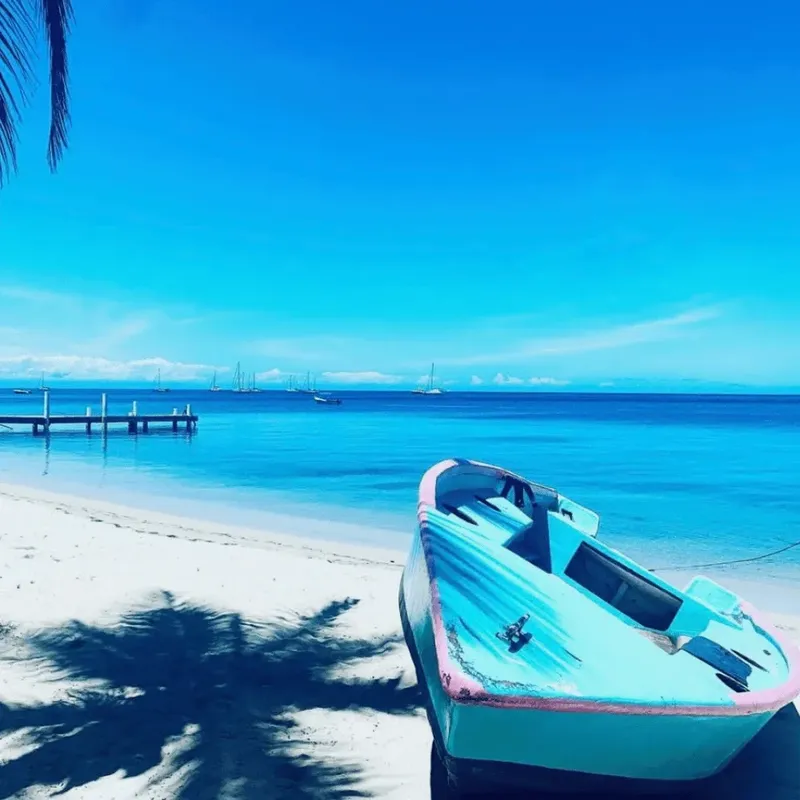 Plage de sable blanc avec un petit bateau bleu et des voiliers
