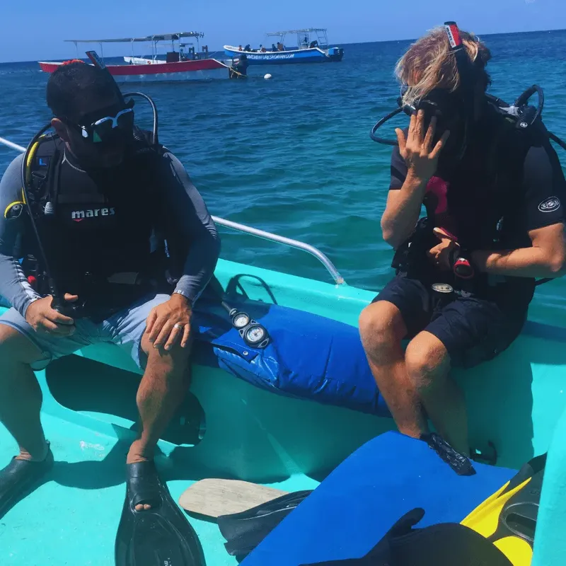 Deux plongeurs équipés assis dans un petit bateau turquoise en mer
