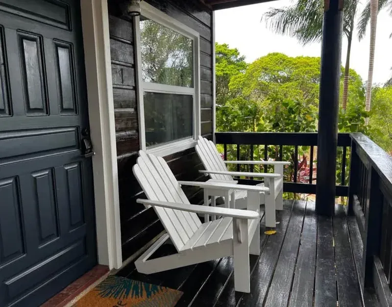Terrasse en bois avec deux chaises blanches devant une porte sombre