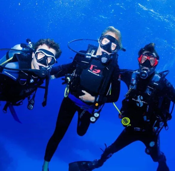 Trois plongeurs souriants en combinaison, masques et détendeurs dans l'eau