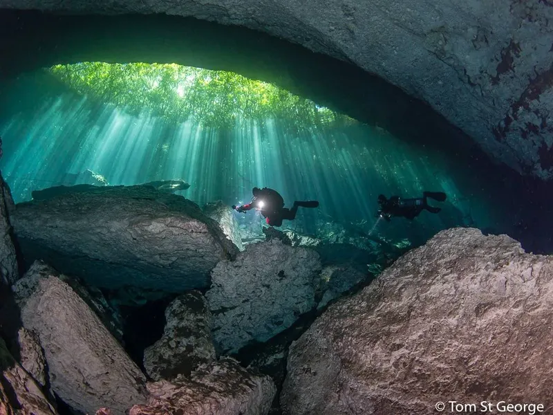 Deux plongeurs explorent une grotte sous-marine éclairée par des rayons de soleil
