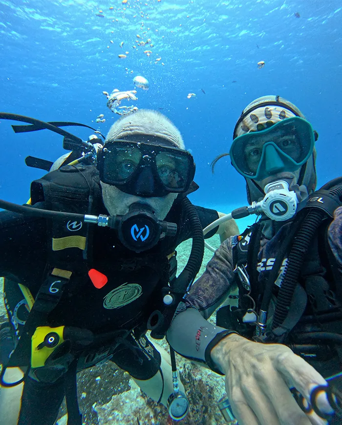 Deux plongeurs souriants avec leur équipement complet dans l'eau bleue