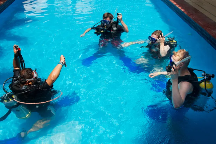Quatre plongeurs s'entrainent en piscine avec leur équipement complet