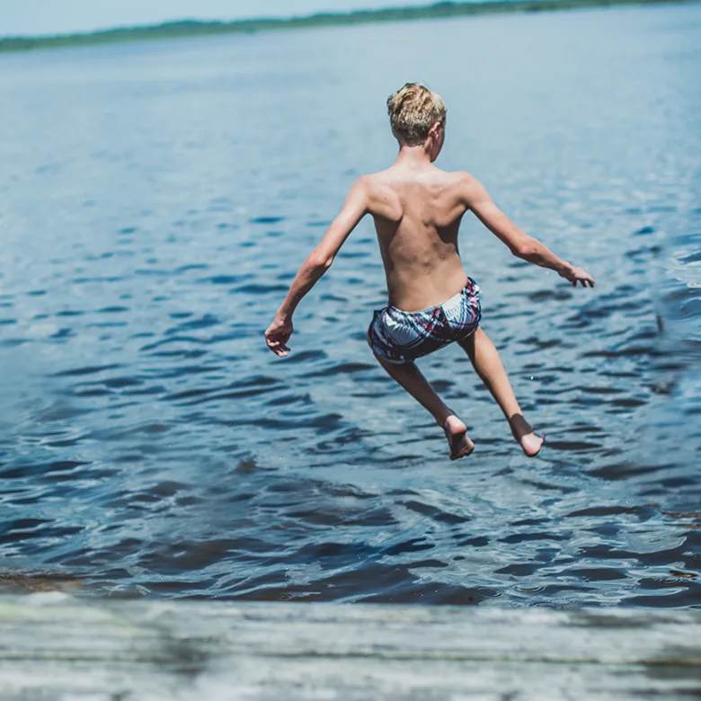 Un jeune homme saute dans l'eau claire, en maillot de bain