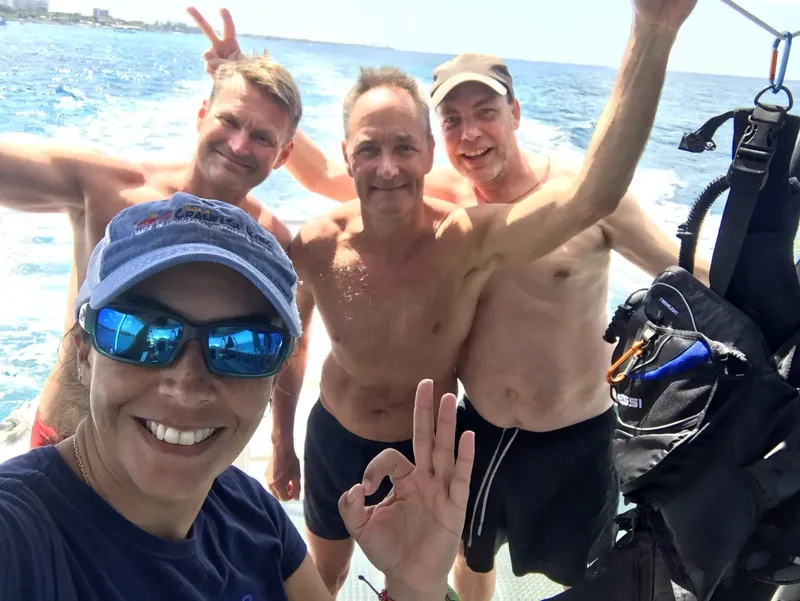 Quatre plongeurs souriants sur un bateau en mer, équipement visible