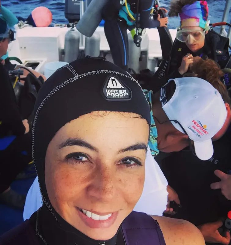 Plongeuse souriante sur un bateau avec d'autres plongeurs équipés