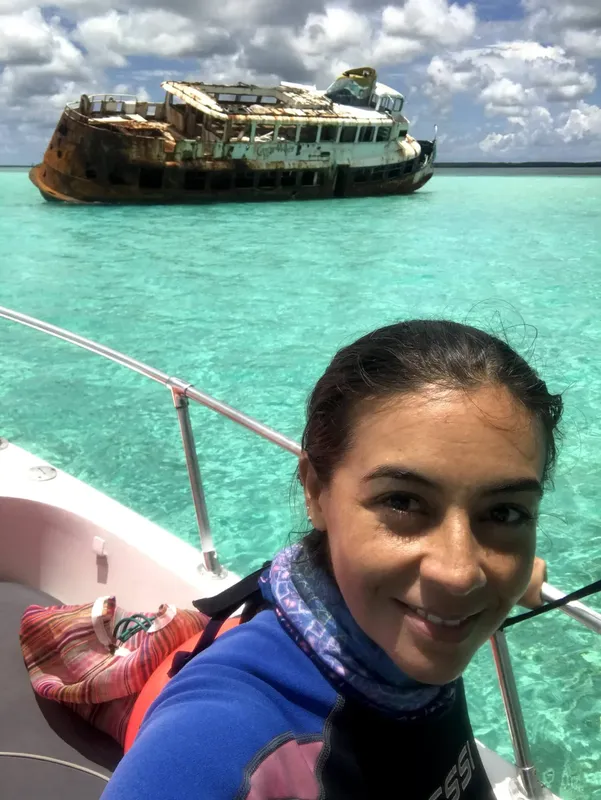 Jeune femme souriante sur un bateau devant une épave rouillée