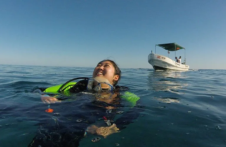 Plongeuse souriante à la surface avec bateau en arrière-plan