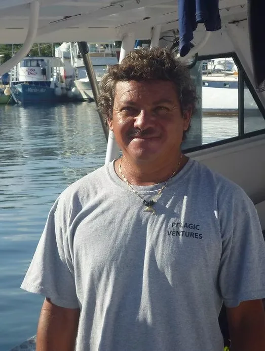 Homme souriant près d'un bateau amarré dans un port ensoleillé